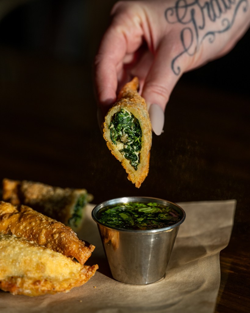 hand dipping an empanada filled with spinach and ricotta