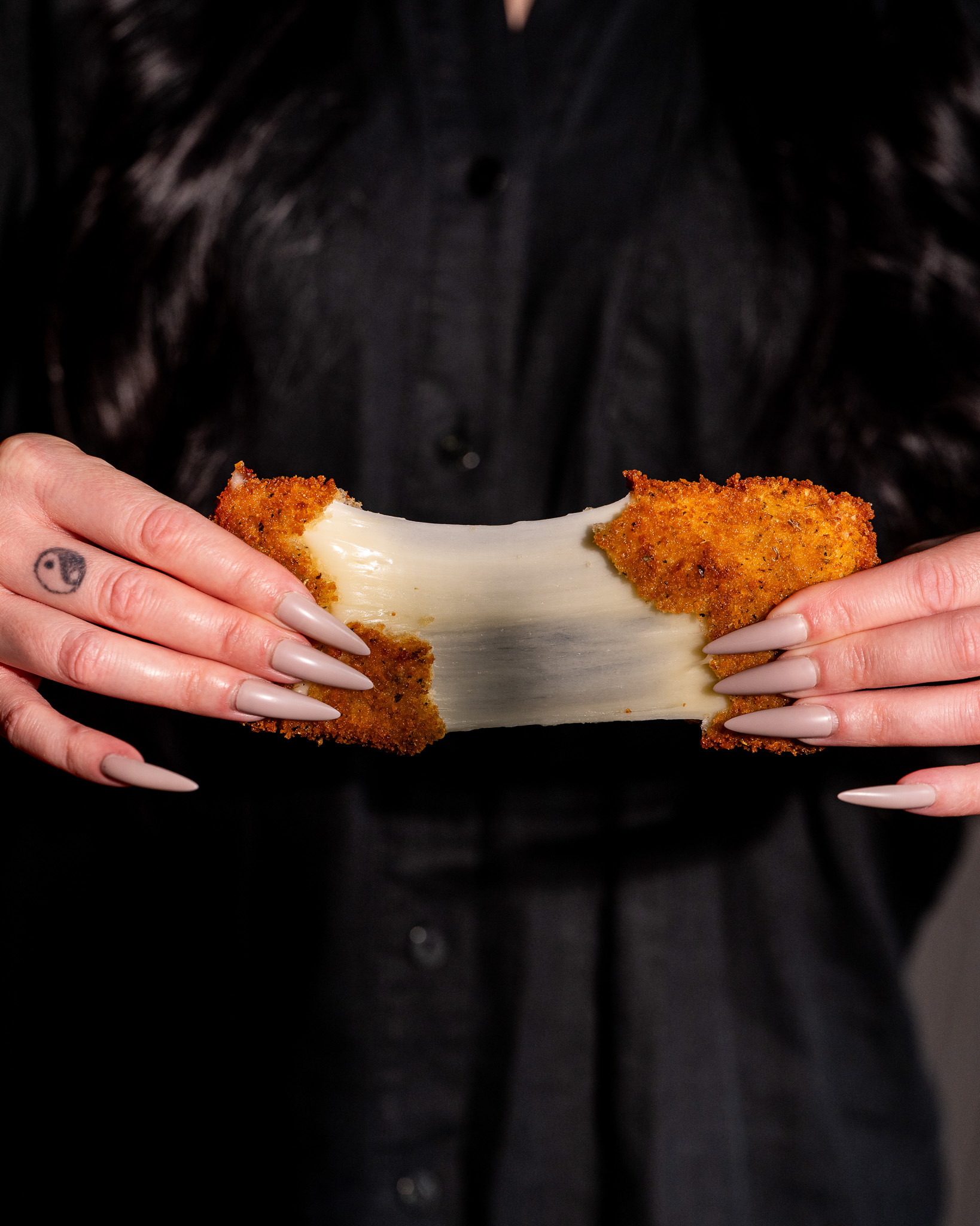 hands pulling apart a fried mozzarella square with cheese stretching between hands