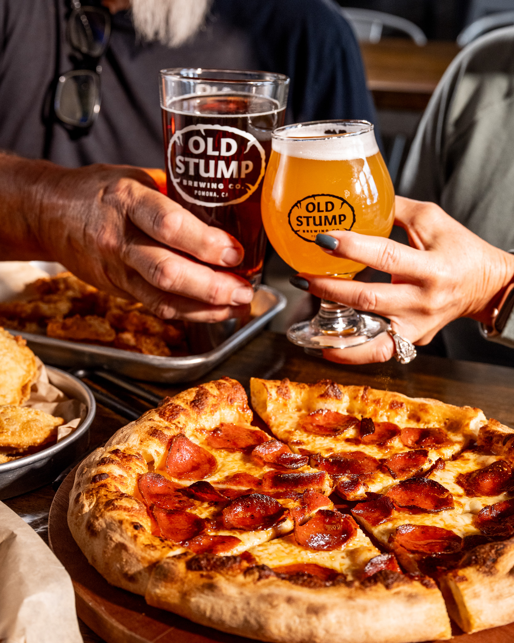 two old stump beer glasses clinking in front of fresh pepperoni pizza