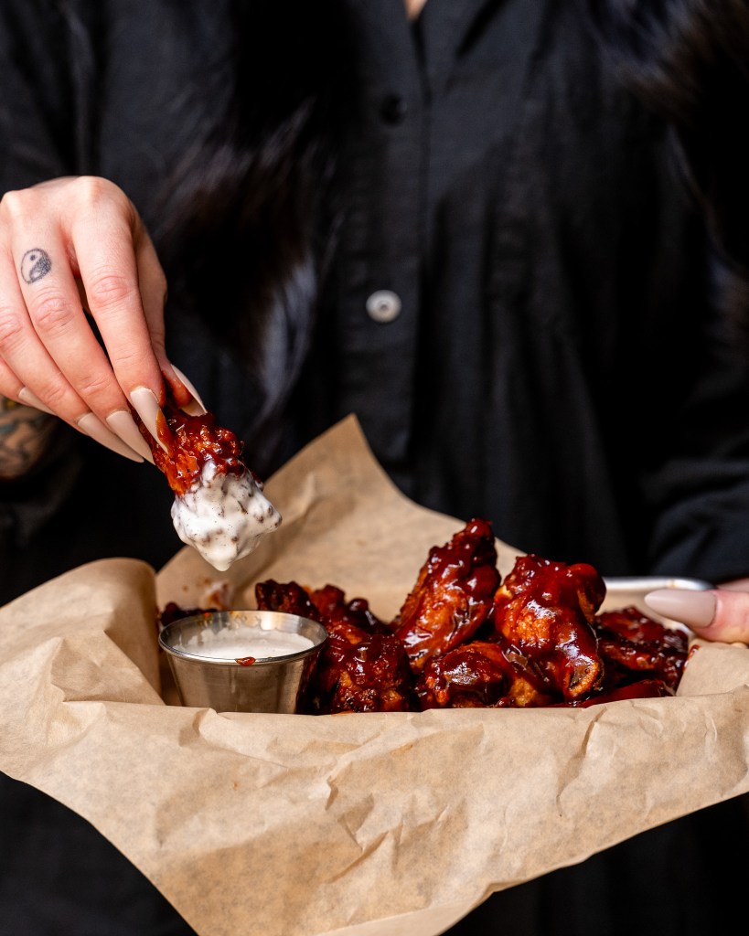 hand dipping bone-in barbecue wings into a side of ranch